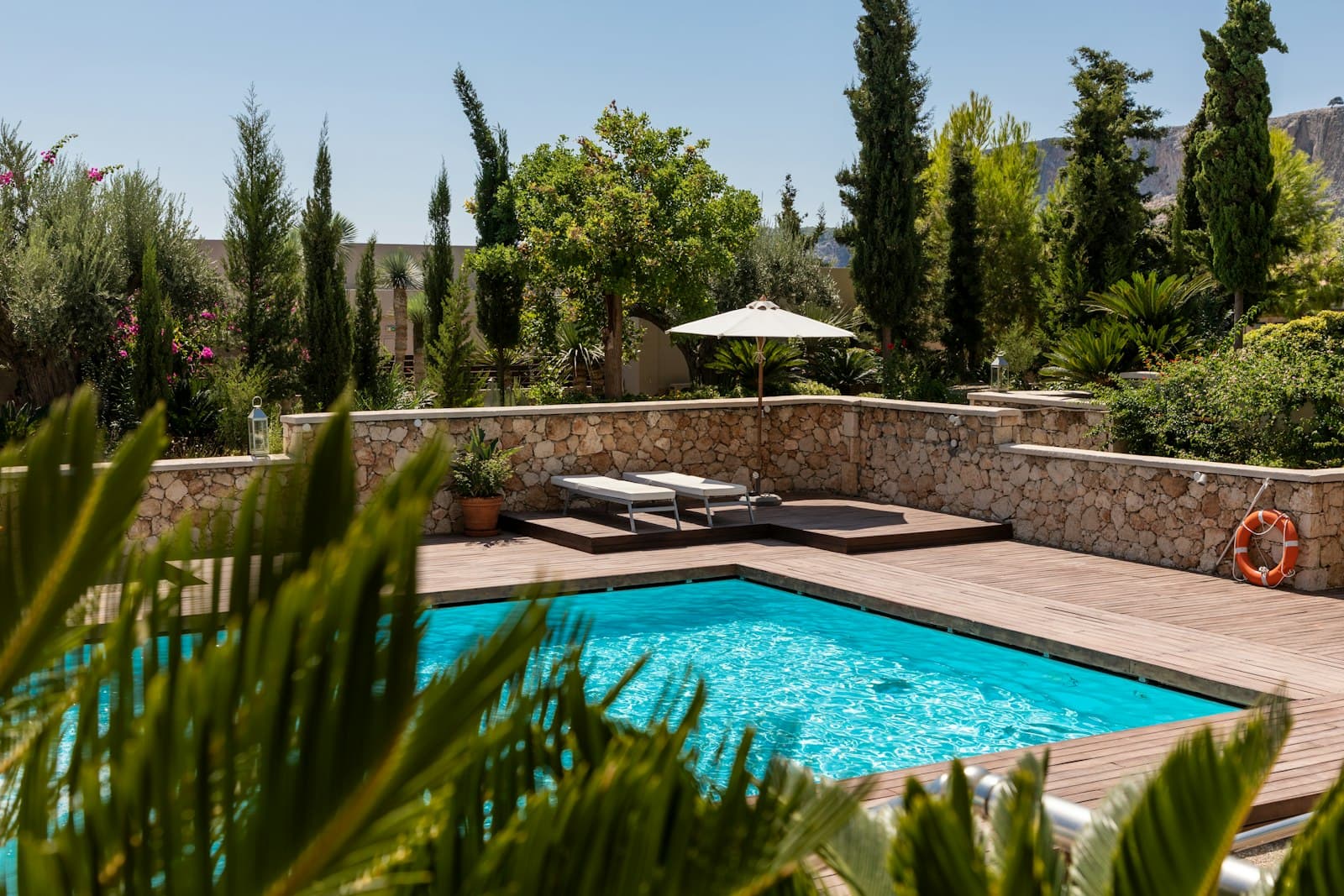 A tidy residential backyard pool with a stone patio and umbrella